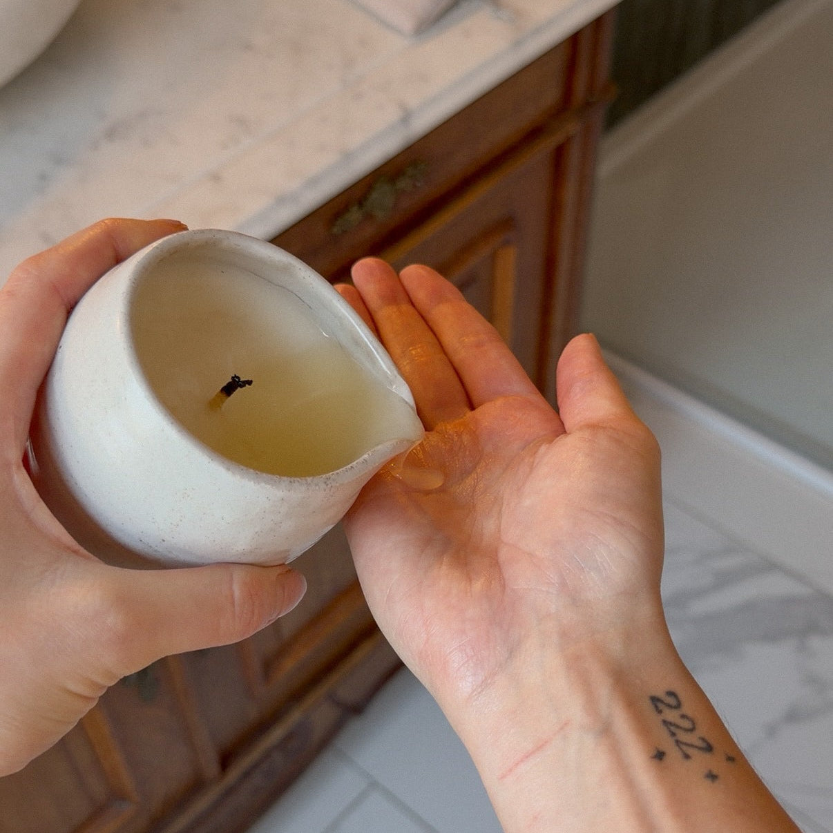 Person holding a small ceramic container with a candle inside on a bathroom counter.